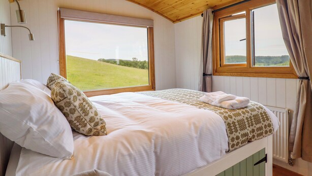 A bedroom with a bed, a window with a view of a green field, and wooden ceiling beams. - Defaid Cymreig (Oswestry)