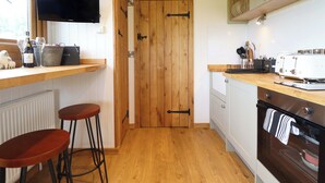 A kitchen with wooden cabinets, a built-in oven, a television, and two bar stools. - Defaid Cymreig (Oswestry)