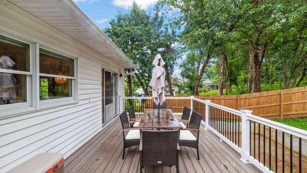 A wooden deck with a table and chairs, a covered umbrella, and a view of a wooded area.