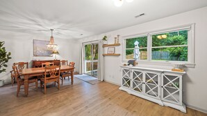 A dining room with a wooden table and chairs, a chandelier, and a window with a view of greenery.