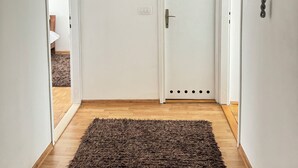 A hallway with a wooden floor, a dark brown rug, a white door, and a framed picture on the wall. - Charming 1-bedroom apartment in brilliant Sarajevo with WiFi, AC (Sarajevo)