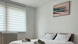 A bedroom with a wooden bed, white bedding, a radiator, a window with blinds, and a painting on the wall. - Charming 1-bedroom apartment in brilliant Sarajevo with WiFi, AC (Sarajevo)