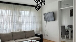 A modern living room with a sectional sofa, a glass coffee table, and a TV mounted on the wall. - Charming 1-bedroom apartment in brilliant Sarajevo with WiFi, AC (Sarajevo)