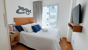 Una habitación de hotel con cama, televisión, ventana y una obra de arte en la pared.