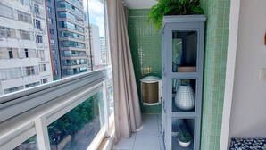 Un balcón con vistas a edificios altos, una planta en maceta, un estante con adornos y un espejo fijado a la pared.