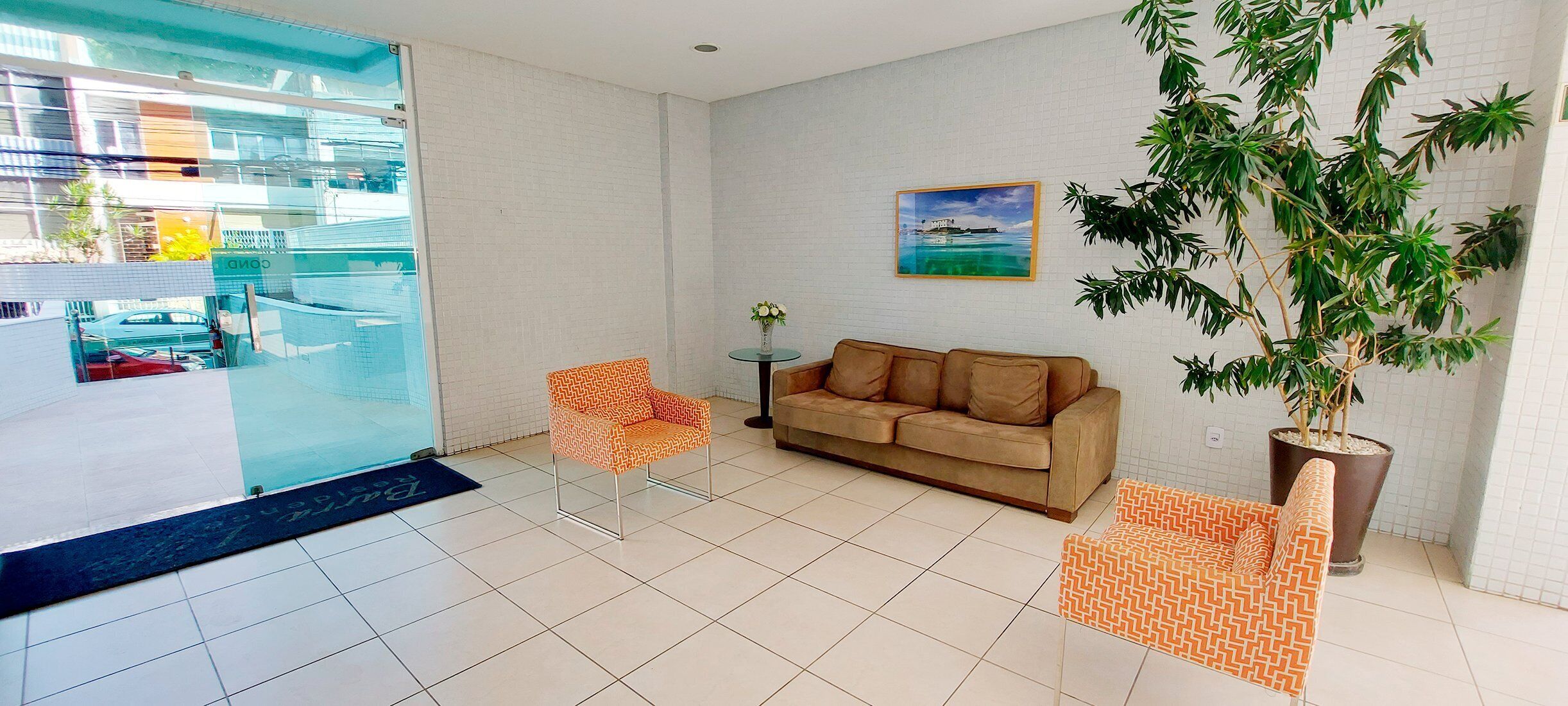Un salon moderne avec une porte vitrée donnant sur une piscine, un canapé marron, deux fauteuils à motifs, une plante en pot et un tableau encadré au mur.