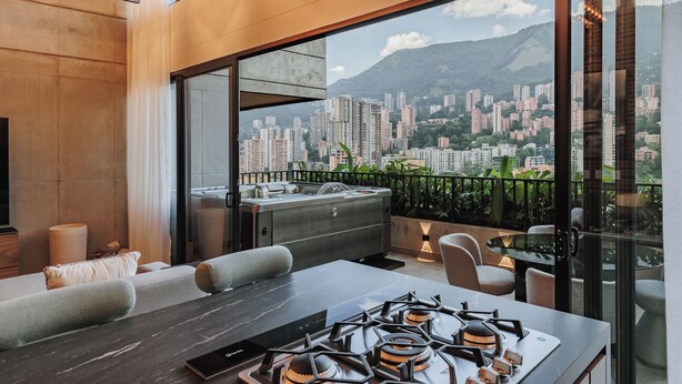 A modern kitchen with a gas stove, a dining area with a table and chairs, and a large window offering a city view. - Morph by MOME Stays (Medellín)
