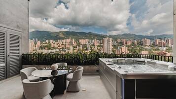 Ein Balkon mit Whirlpool, Tisch und Stühlen, mit Blick auf eine Skyline mit zahlreichen Gebäuden und Bergen.