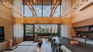 A modern living room with a large window, a kitchen area, and a seating area with a long table. - Morph by MOME Stays (Medellín)