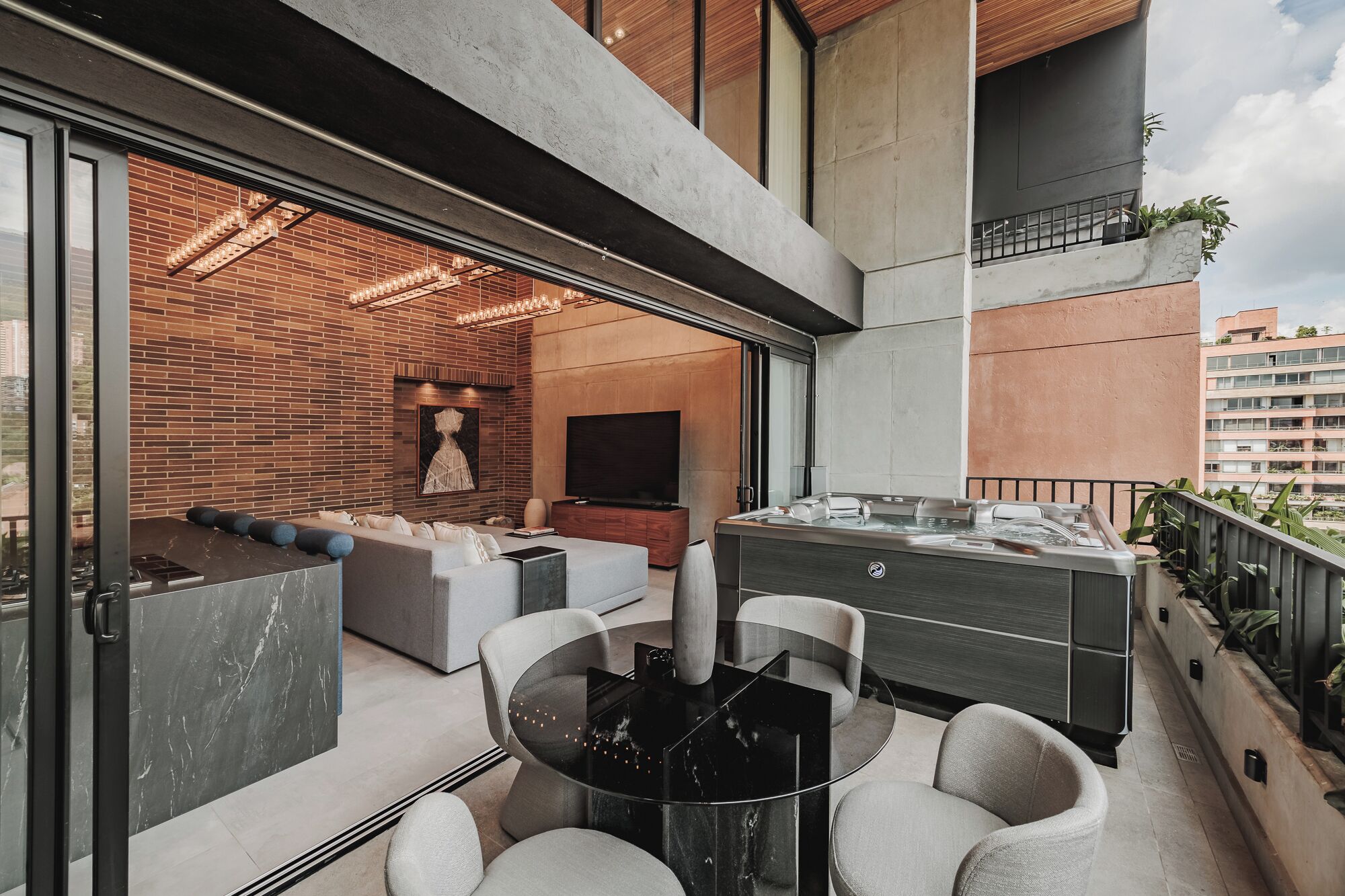 A modern balcony with a glass door leading to a living area, a hot tub, and a seating area with a table and chairs.