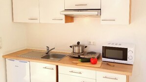 A compact kitchen with white cabinets, a sink, a stove, a microwave, and a small refrigerator. - Vacation apartments on the Lesum - FeWo Lesmona - TOP long-term conditions (Bremen)
