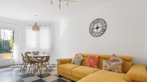 A living room with a yellow sofa, checkered floor, and a wall clock.