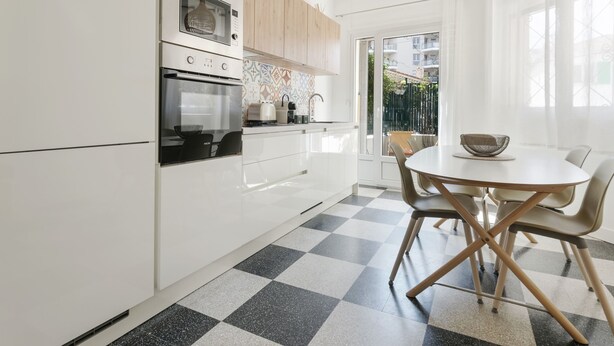 A modern kitchen with white cabinets, a black and white checkered floor, and a dining area with a round table and chairs.