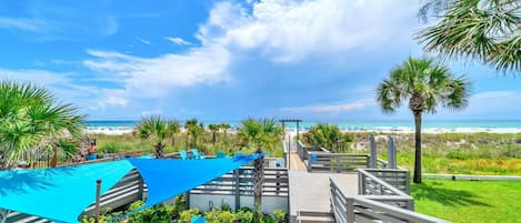 A beachside walkway with a view of the ocean, palm trees, and beach umbrellas.