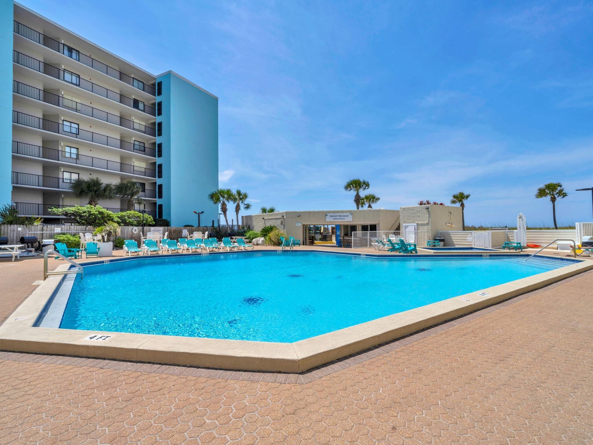 A swimming pool with lounge chairs, a building with balconies, and palm trees.