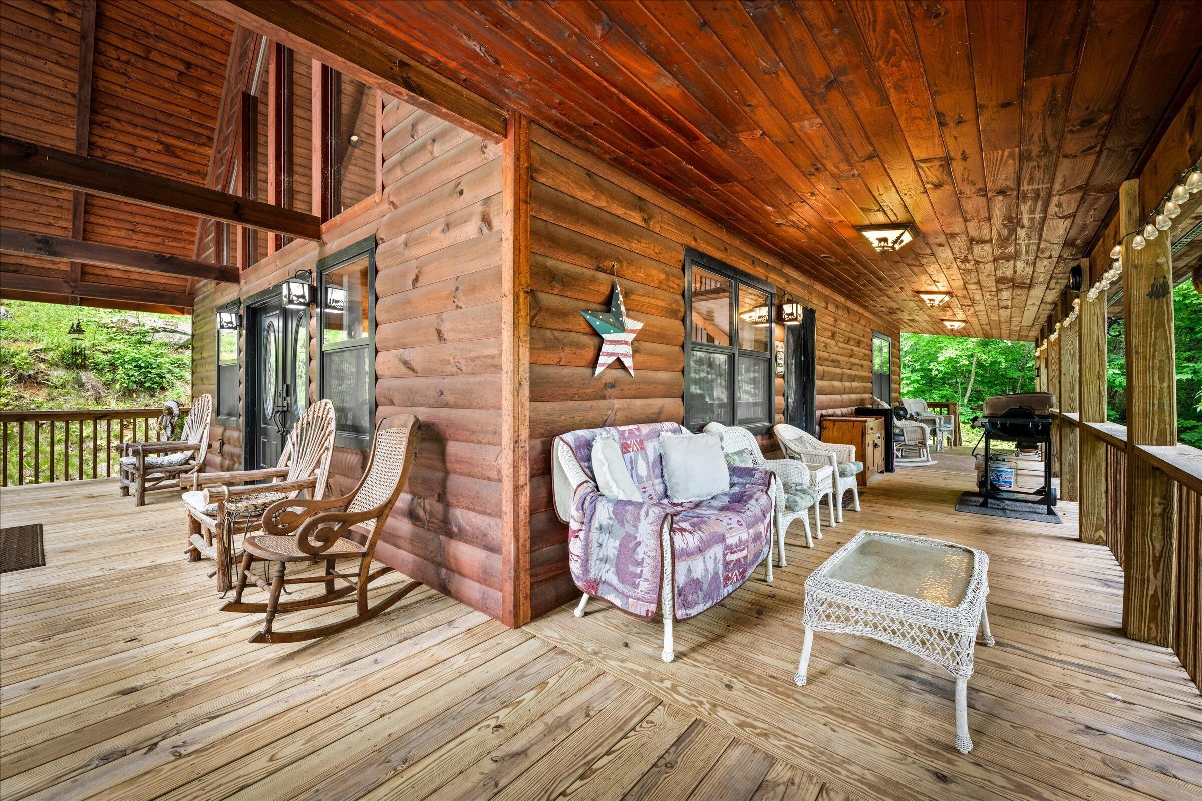 A wooden cabin with a porch, rocking chairs, a cushioned bench, and a table.
