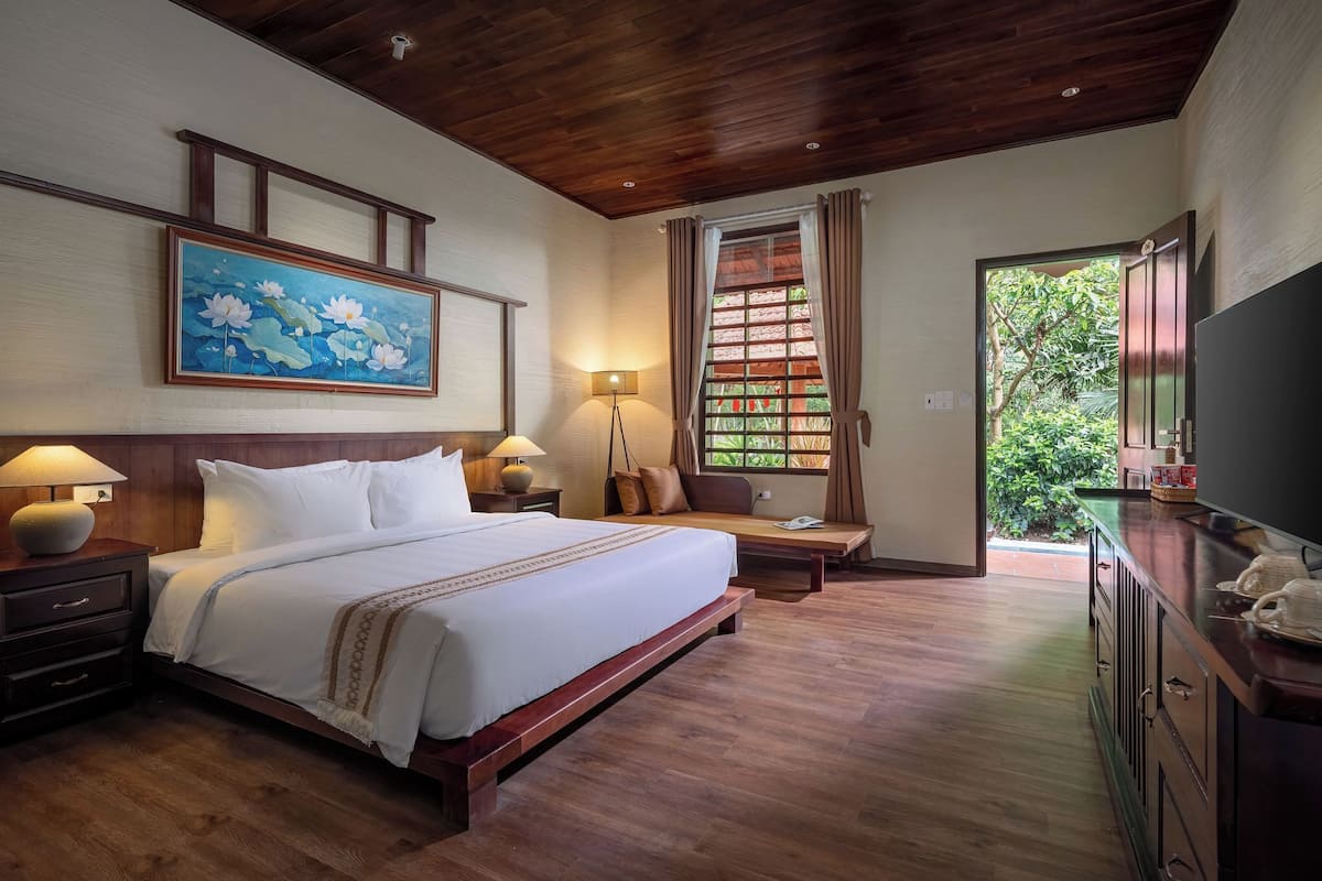 A hotel room with a wooden bed, bedside tables, a desk, a television, and a window with curtains.