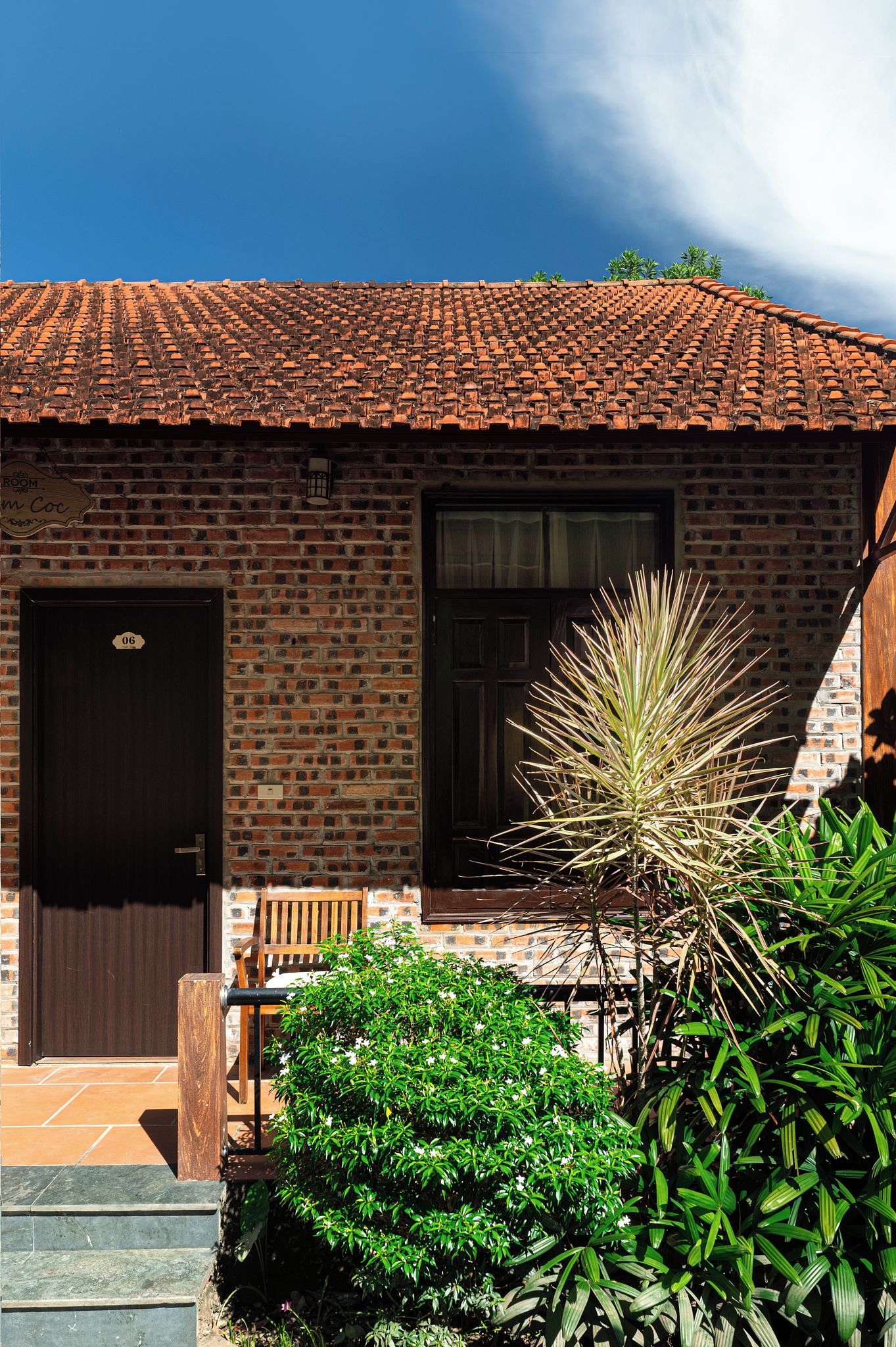 A brick building with a tiled roof, a wooden door, and a bench outside.
