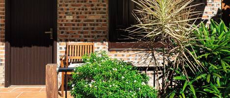 A brick building with a tiled roof, a wooden door, and a bench outside.