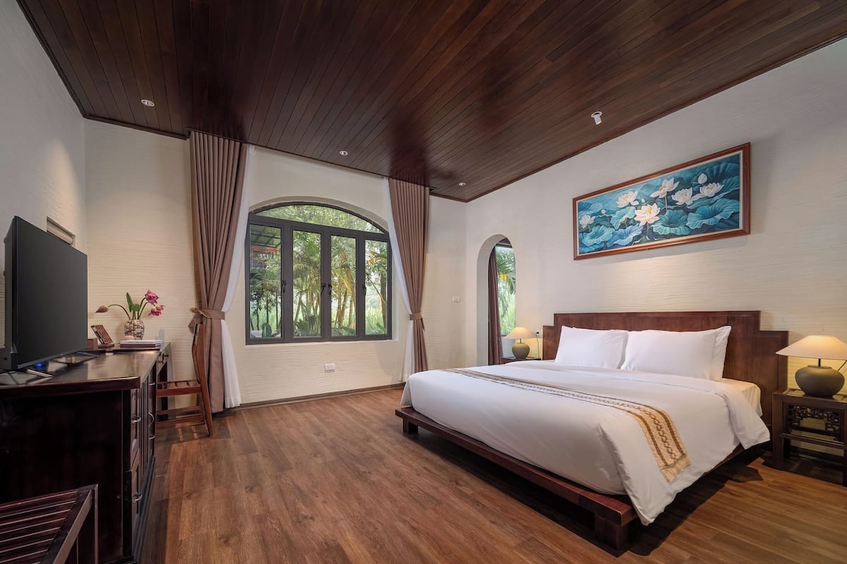 A spacious bedroom with a large bed, wooden flooring, a TV, and a painting of lotus flowers.