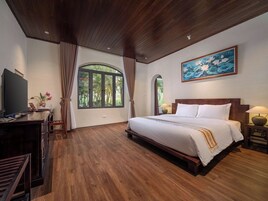 Un dormitorio amplio con una cama grande, suelo de madera, un televisor y un cuadro de flores de loto.