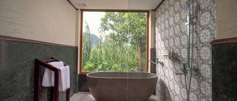 A bathroom with a freestanding bathtub, a shower, and a large window offering a view of greenery.