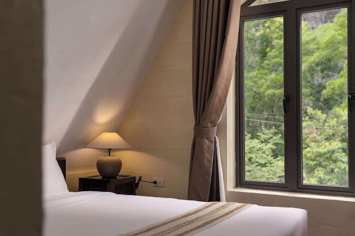 A bedroom with a bed, a nightstand with a lamp, and a window with curtains.