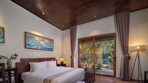 A hotel room with a wooden ceiling, a large bed with white bedding, a bench, a bedside table with a lamp, a painting on the wall, and a view of greenery through a sliding door. - Mua Valley Lodge (Ninh Binh)
