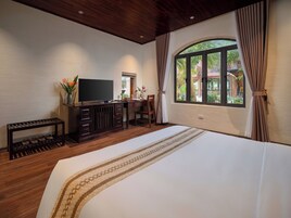 Un dormitorio con una cama grande, televisor, escritorio y ventana con cortinas.