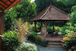 Ein Pavillon mit einem Ziegeldach, umgeben von üppiger Vegetation und einem Steinweg.