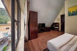 Une chambre d’hôtel avec un grand lit, un plancher en bois, une télévision et une vue sur une piscine et la verdure environnante.
