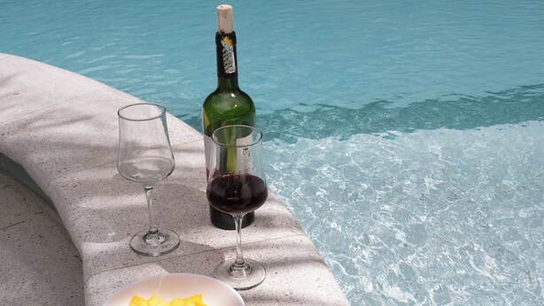 Une table placée au bord de la piscine, avec une bouteille de vin, deux verres et un saladier de fruits.