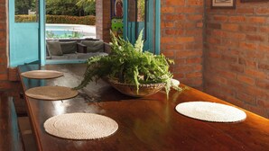 Un coin repas avec une table en bois, des sets de table en fibres tressées et une plante en pot.