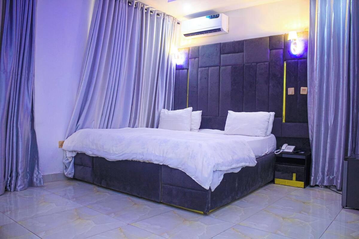 A bedroom with a large bed, a bedside telephone, and an air conditioning unit.