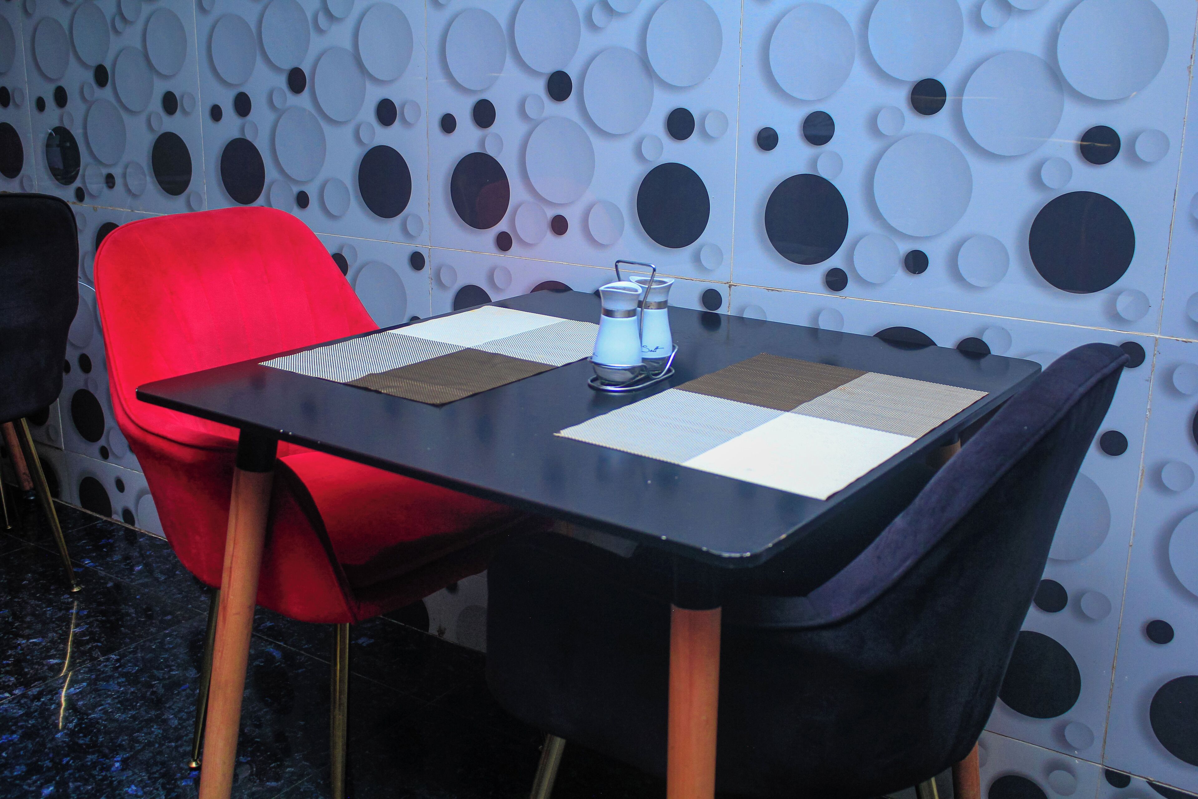 Un tavolo con piano nero, circondato da sedie rosse e nere, addossato a un muro decorato con un motivo circolare.