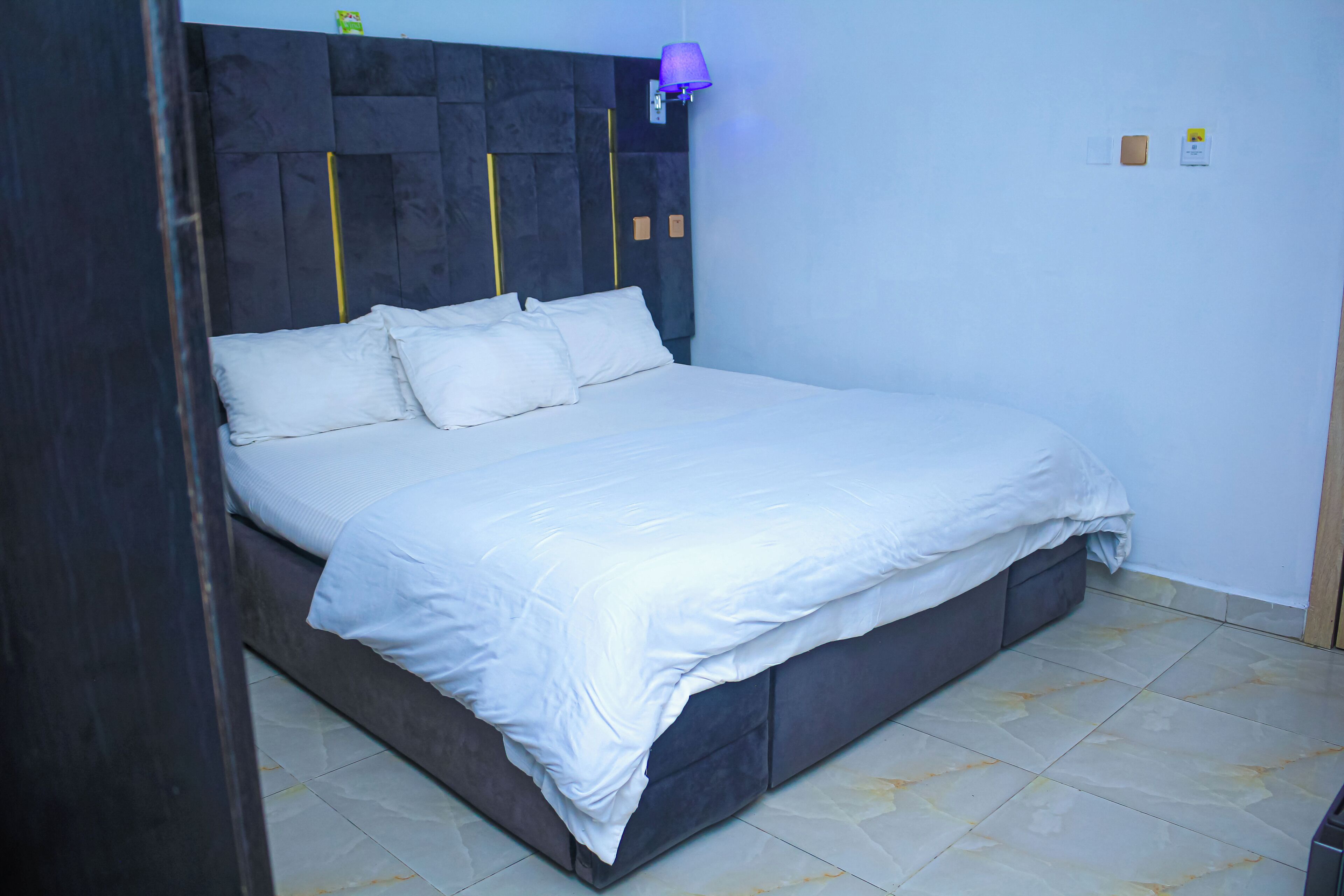 A neatly made bed with white linens in a room with a dark headboard and a wall-mounted lamp.