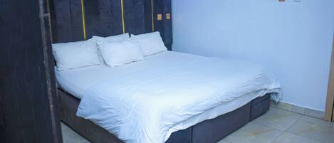 A neatly made bed with white linens in a room with a dark headboard and a wall-mounted lamp.