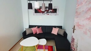 A modern living room with a black sofa, two white tables, a colorful rug, and a large abstract painting above the sofa. - Cozy vacation apartment Berlin for 9 people (Berlin)