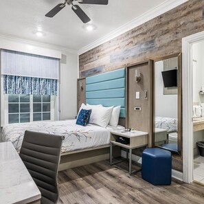 A hotel room with a bed, bedside table, chair, and a television on a wall. - Greenleaf Hotel (Long Beach)