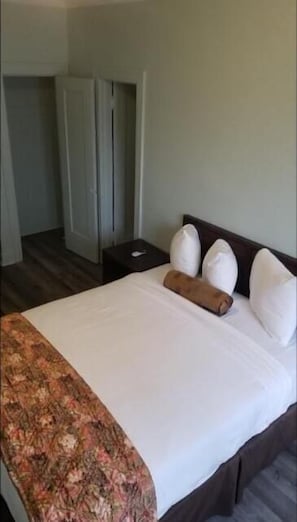 Un lit bien fait, recouvert d’une couvre-lit à motifs floraux, avec une tête de lit en bois et une table de chevet surmontée d’une lampe.