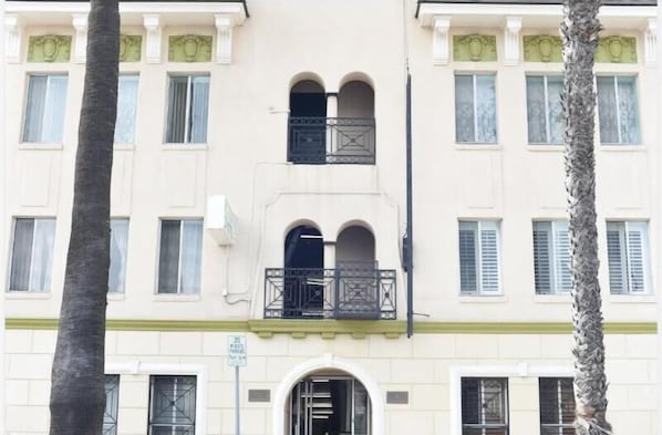 Un immeuble à plusieurs étages doté d’une façade symétrique, avec des fenêtres en arc de cercle et des balcons ornés de garde-corps en métal.