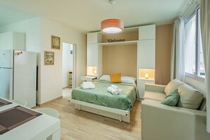 A hotel room with a bed, a sofa, a desk, and a refrigerator.