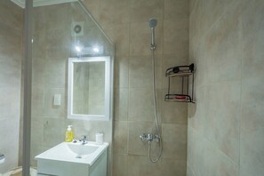 A bathroom with a shower, a sink, a mirror, and a shelf with toiletries.