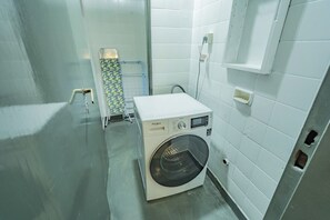 A compact laundry room with a front-loading washing machine, a drying rack, and a small shelf unit. - Spacious Apartment in Downtown Buenos Aires (Buenos Aires)