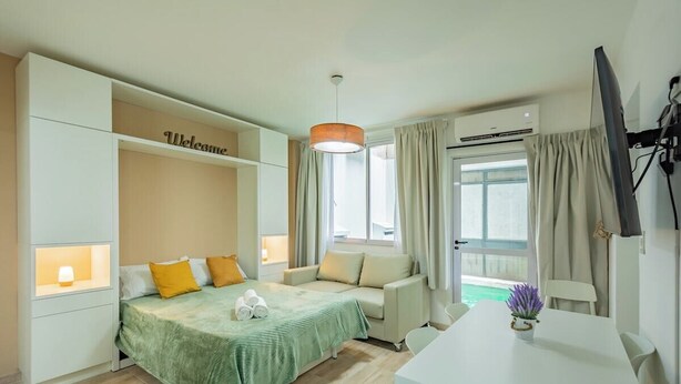 Ett hotellrum med en säng, en soffa, ett matbord, en tv och ett fönster med gardiner.