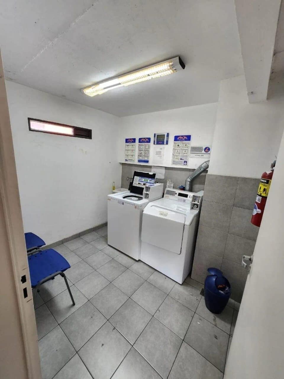 A laundry room with a washing machine, dryer, and a blue chair.