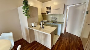 A compact kitchen with a small island, a toaster, a kettle, and a hanging plant.