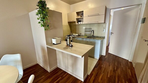 A compact kitchen with a small island, a toaster, a kettle, and a hanging plant.