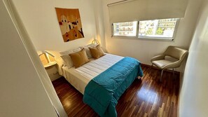 A bedroom with a bed, a chair, a nightstand, a window, and a painting on the wall. - Luxury Apartment in Belgrano (Buenos Aires)
