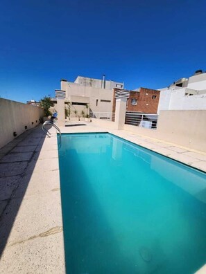A rooftop swimming pool with a clear blue sky above, surrounded by buildings.